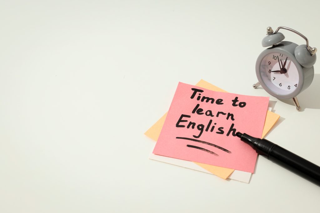 Nota con texto "Time to learn English" junto a un bolígrafo y un reloj.